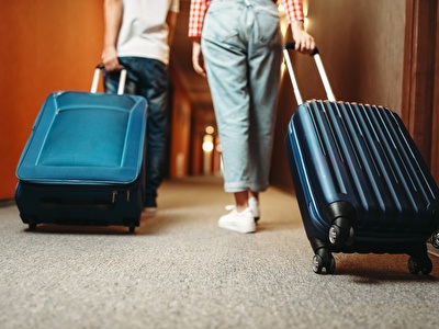 Couple walks down hotel hallway with suitcases to room