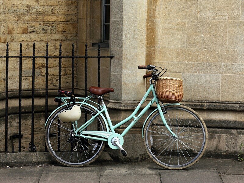 Een licht groene fiets geparkeerd op de stoep leunend tegen een stenen muur.